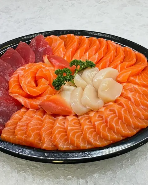 Salmon sashimi fanned in a round black tray with scallops
