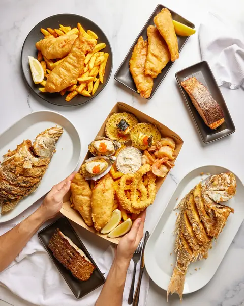 Fish and chips, fried fish, chips and fried seafood shared by hands at the table