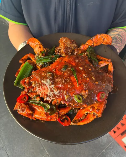Chilli crab on a black plate held up to the camera
